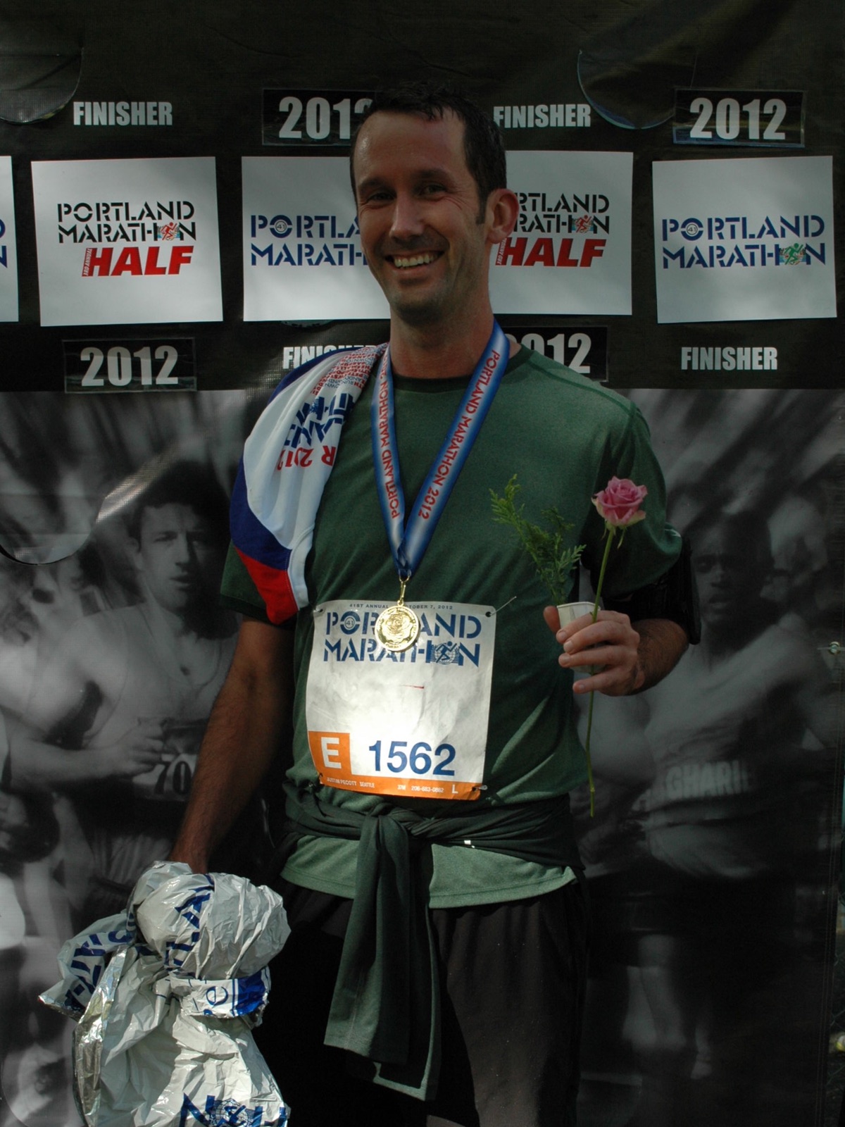 Justin beaming at the finish line of the 2012 Portland Marathon Half, wearing his medal and holding a pink rose and his finisher's bag